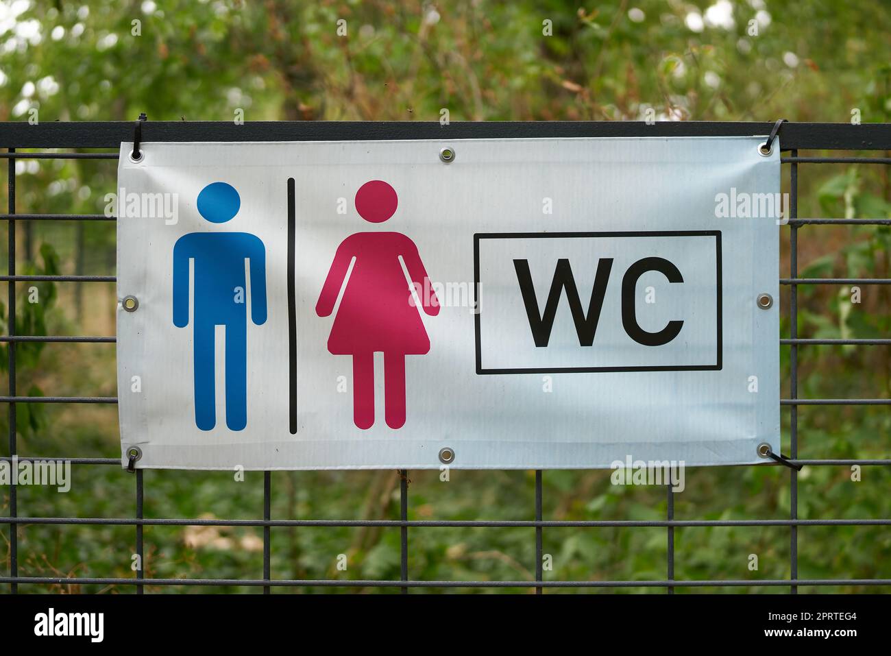 Hinweis auf eine Toilette in der Nähe durch ein Schild an einem Zaun in einem Park in Deutschland Stockfoto
