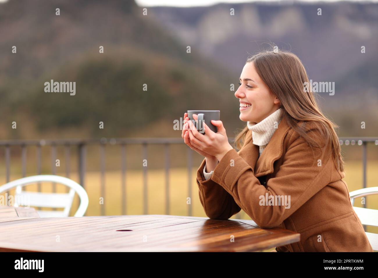 Glückliche Frau im Winter, die auf der Terrasse trinkt Stockfoto