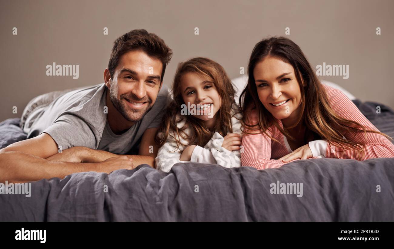 Bequeme Klebezeit. Porträt einer glücklichen Familie, die sich auf einem Bett entspannt. Stockfoto