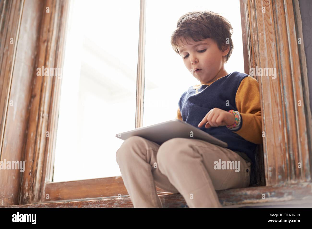 HES Tech-versierte bereits. Ein netter kleiner Junge mit einem Tablet, während er auf einer Fensterbank sitzt. Stockfoto