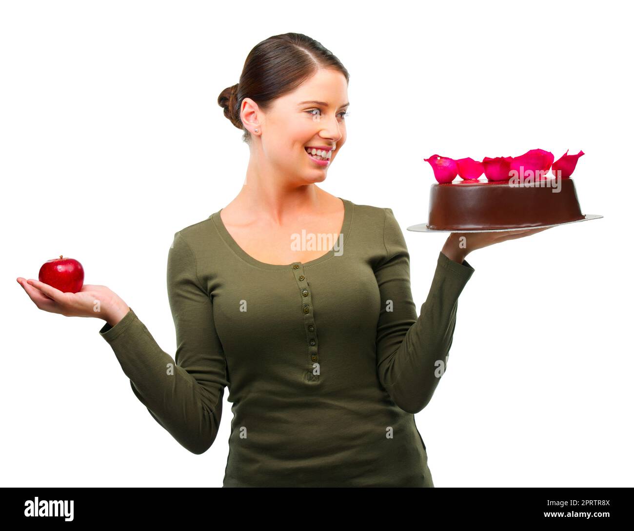 Das Bedürfnis zu frönen. Studioaufnahme einer jungen Frau, die sich zwischen einem Apfel und einem auf Weiß isolierten Kuchen entscheidet. Stockfoto
