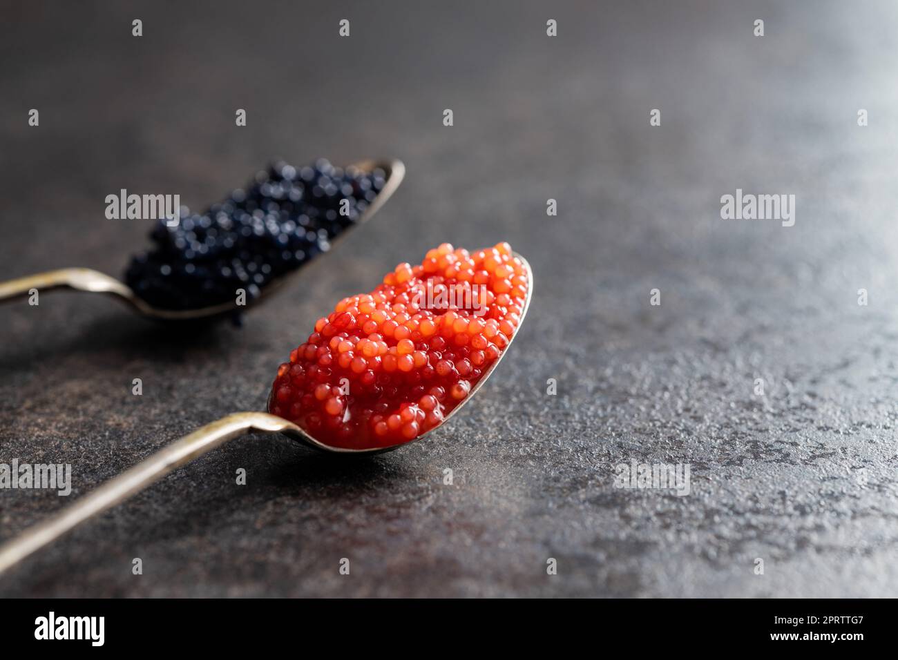 Roter und schwarzer Kaviar in silbernen Löffeln auf einem dunklen Tisch. Stockfoto