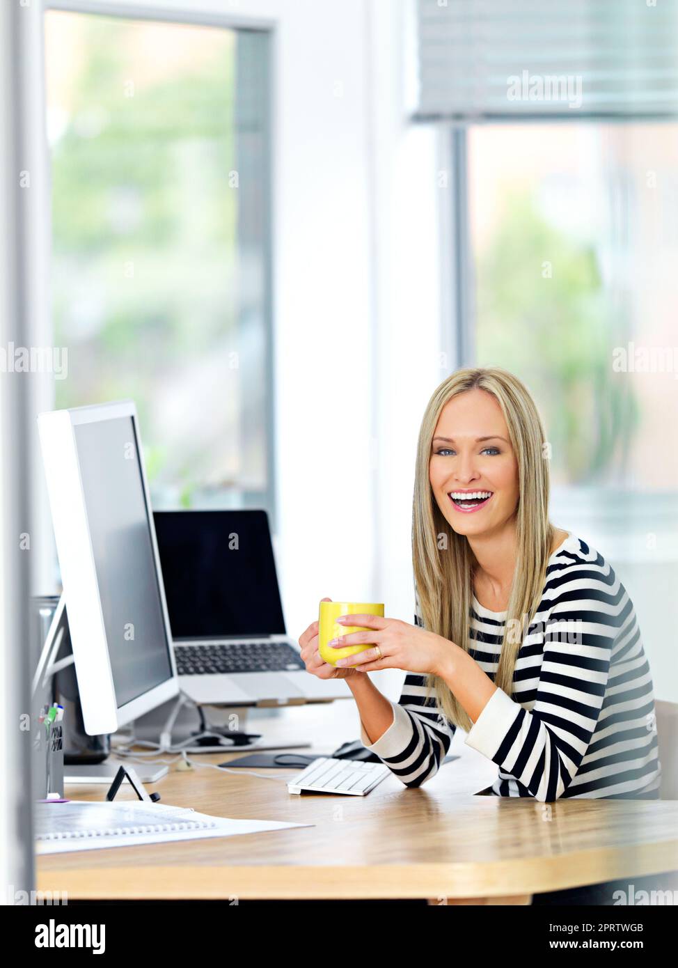 Es gibt immer Zeit für einen Kaffee. Eine schöne junge Frau, die an ihrem Schreibtisch arbeitet, während sie einen Drink genießt. Stockfoto