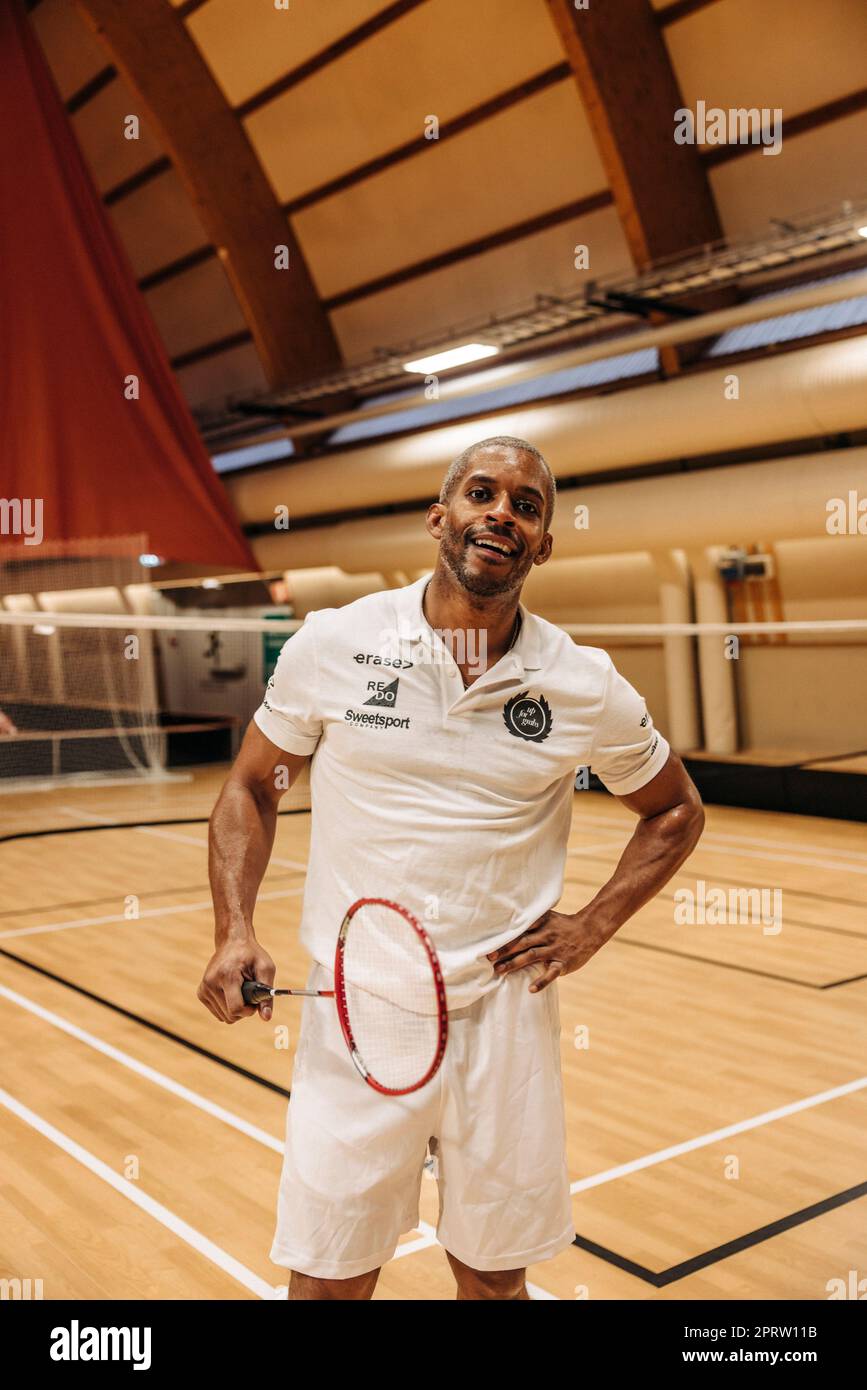 Männlicher Badminton-Spieler, der mit der Hand auf der Hüfte steht, während er auf dem Sportplatz Schläger hält Stockfoto