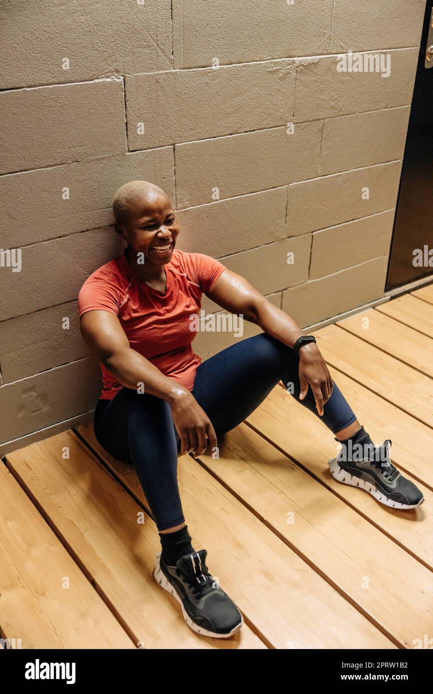 Glückliche Sportlerin, die Pause macht, während sie im Fitnessstudio auf dem Boden sitzt Stockfoto