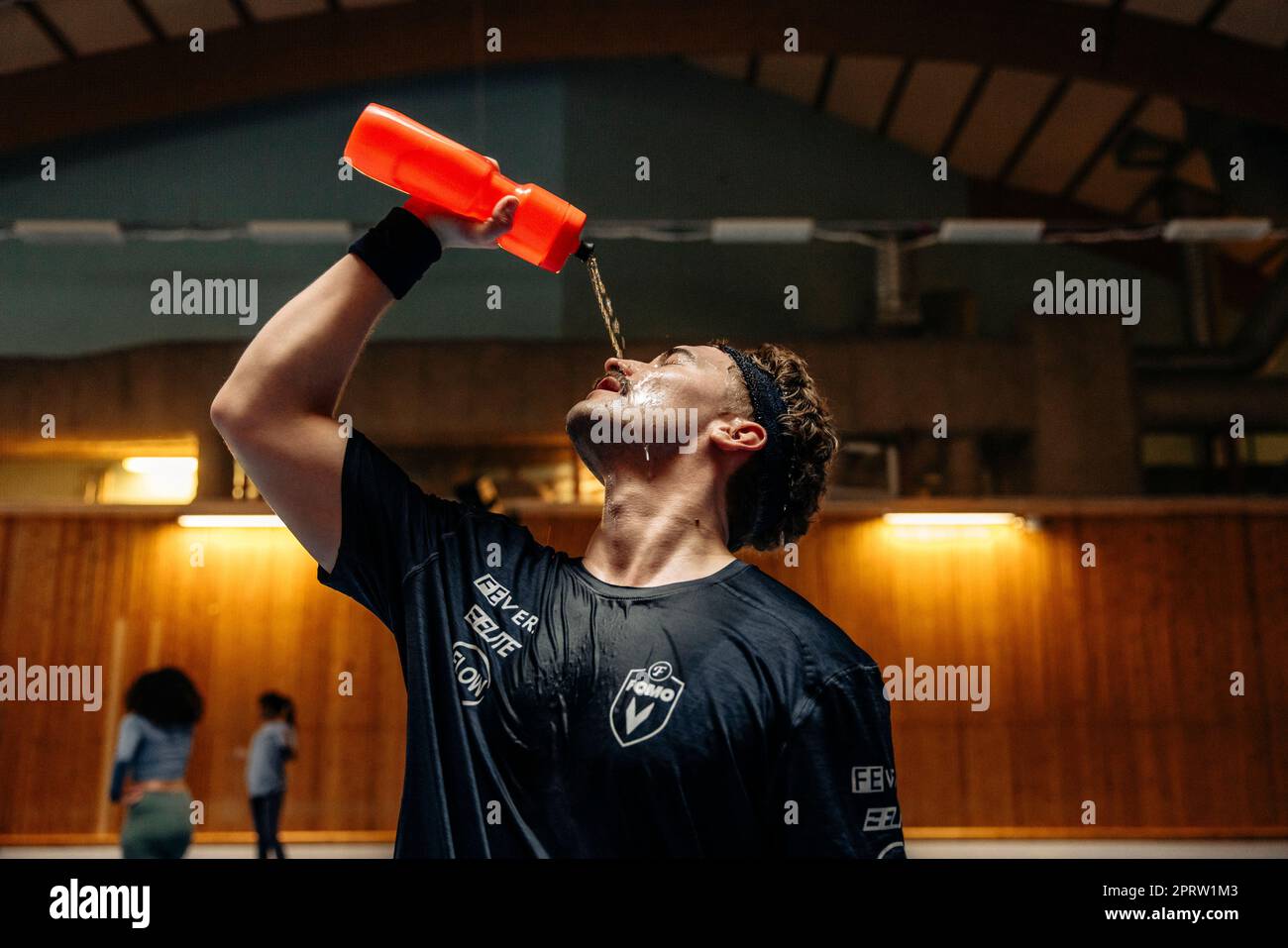 Männlicher Sportler, der auf dem Sportplatz Wasser aus der Flasche ins Gesicht gießt Stockfoto