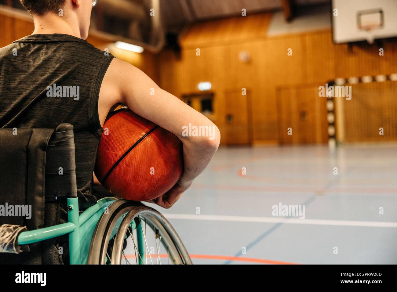 Ein Mädchen, das im Rollstuhl sitzt und Basketball auf dem Sportplatz hält Stockfoto