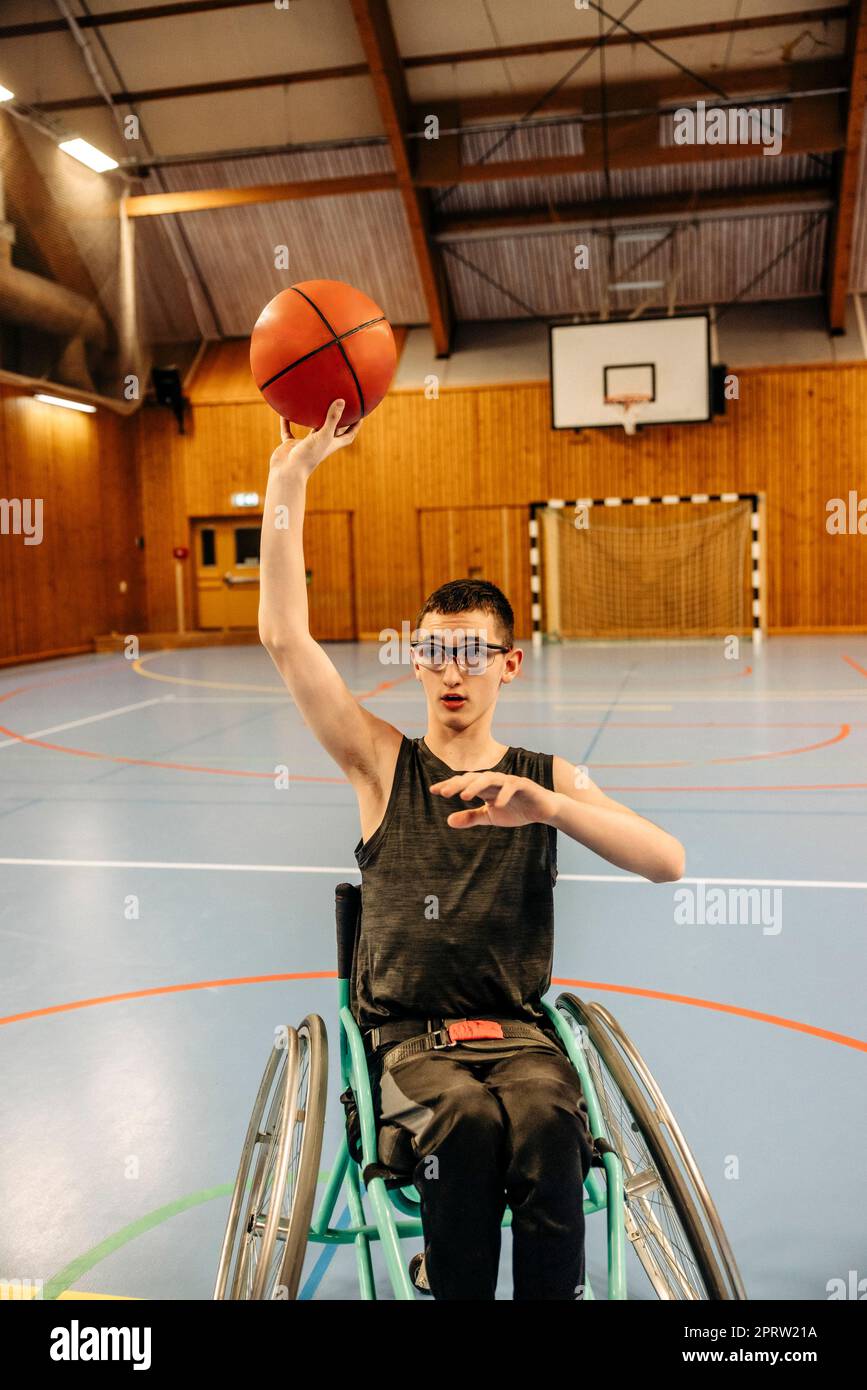 Ein behindertes Mädchen, das Basketball spielt, während es auf dem Rollstuhl auf dem Sportplatz sitzt Stockfoto