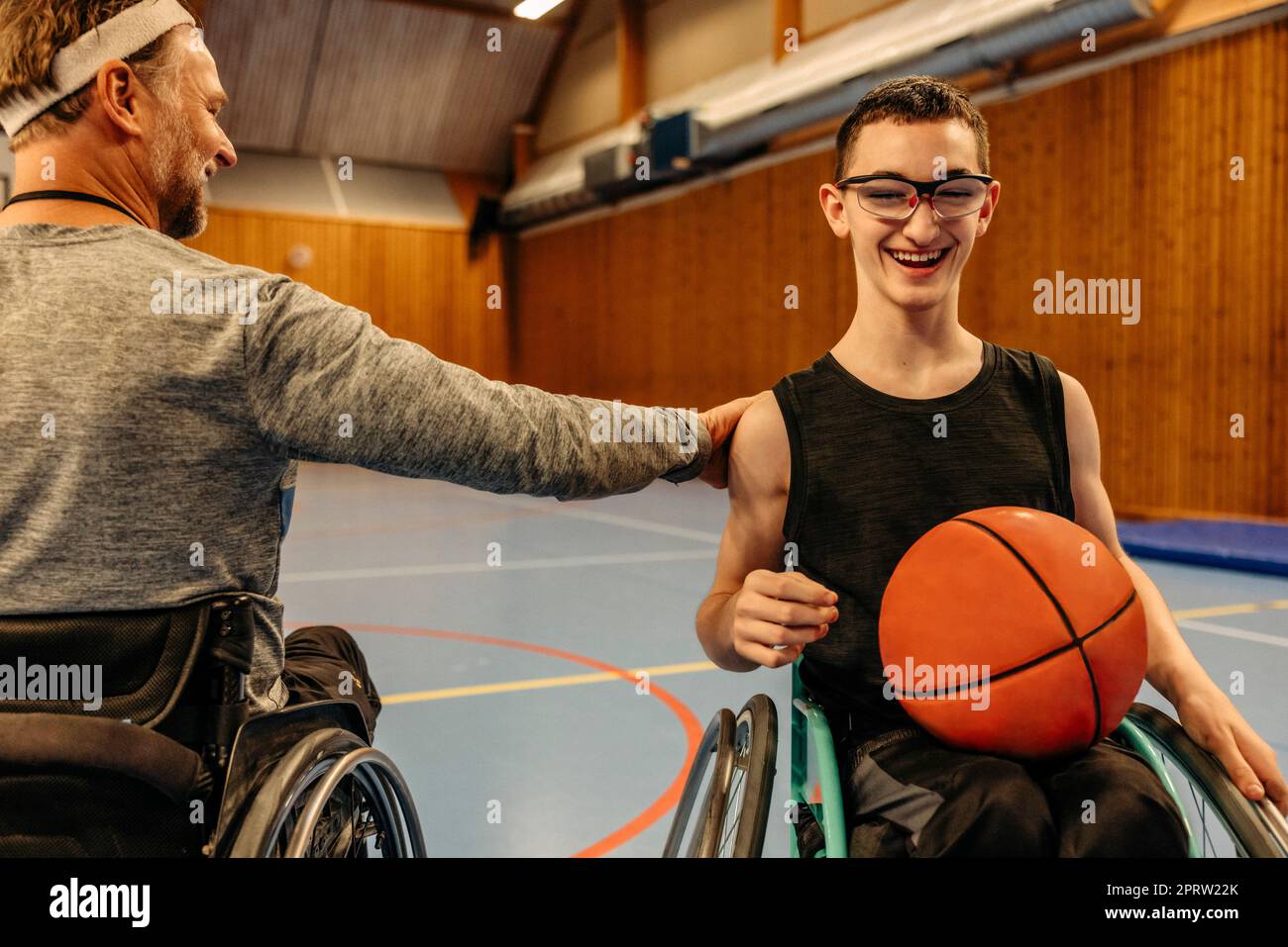 Männlicher Sportler mit behinderungsmotivierendem Mädchen, das im Rollstuhl mit Basketball auf dem Sportplatz sitzt Stockfoto