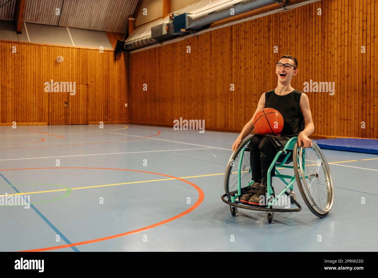 Glückliches Mädchen mit Basketball, das auf dem Rollstuhl auf dem Sportplatz sitzt Stockfoto