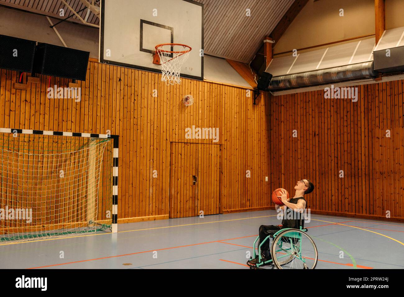 Mädchen, die Basketball spielt, während sie auf dem Sportplatz im Rollstuhl sitzt Stockfoto