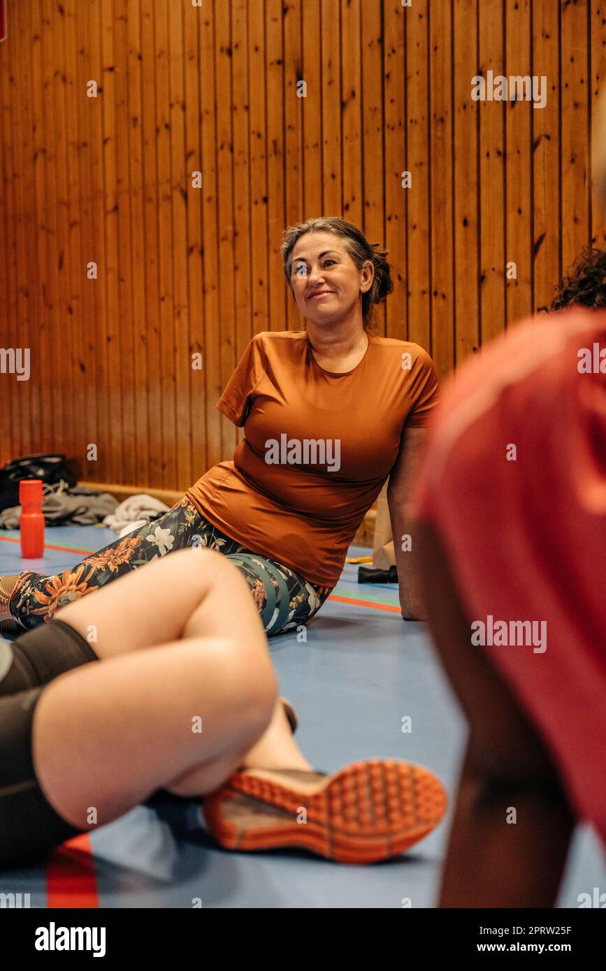 Lächelnde Sportlerin mit Behinderung, die auf dem Boden des Sportplatzes sitzt Stockfoto