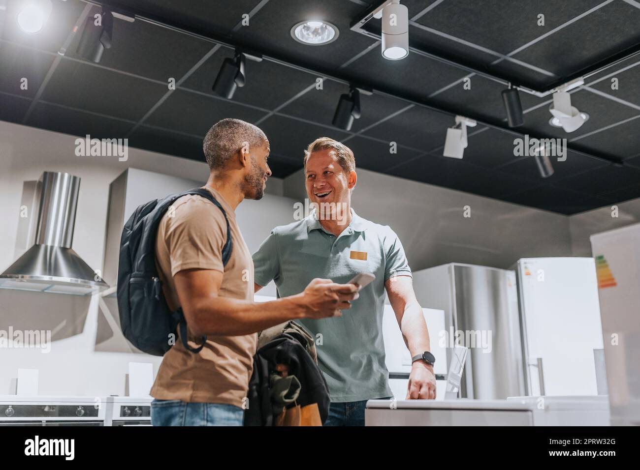 Verkäufer und Kunde lachen, während sie über ein Smartphone im Elektronikgeschäft diskutieren Stockfoto