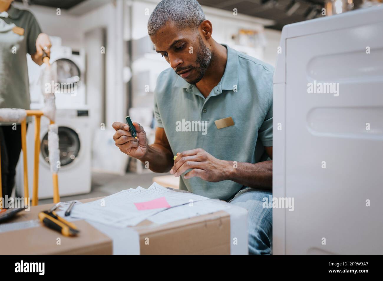 Männlicher Verkäufer, der Papierkram erledigt, während er im Elektronikgeschäft arbeitet Stockfoto