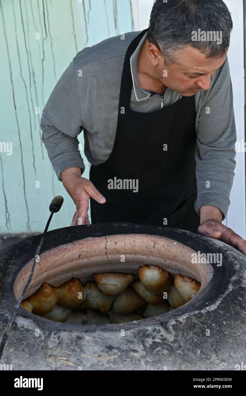 Usbekischer Mann, der in einem Tandir-Ofen in Bukhara, Usbekistan, Somsa, einen traditionellen lokalen Snack, kocht Stockfoto