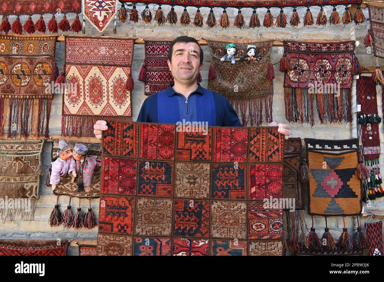 Teppichverkäufer zeigt seine handgefertigten Produkte in seinem Geschäft in Bukhara, Usbekistan Stockfoto