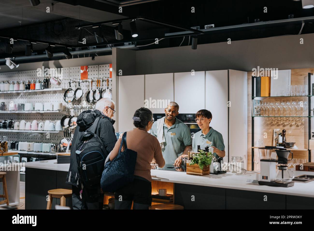 Verkaufsmitarbeiter diskutieren mit Kunden, während sie moderne Küchengeräte im Geschäft verwenden Stockfoto