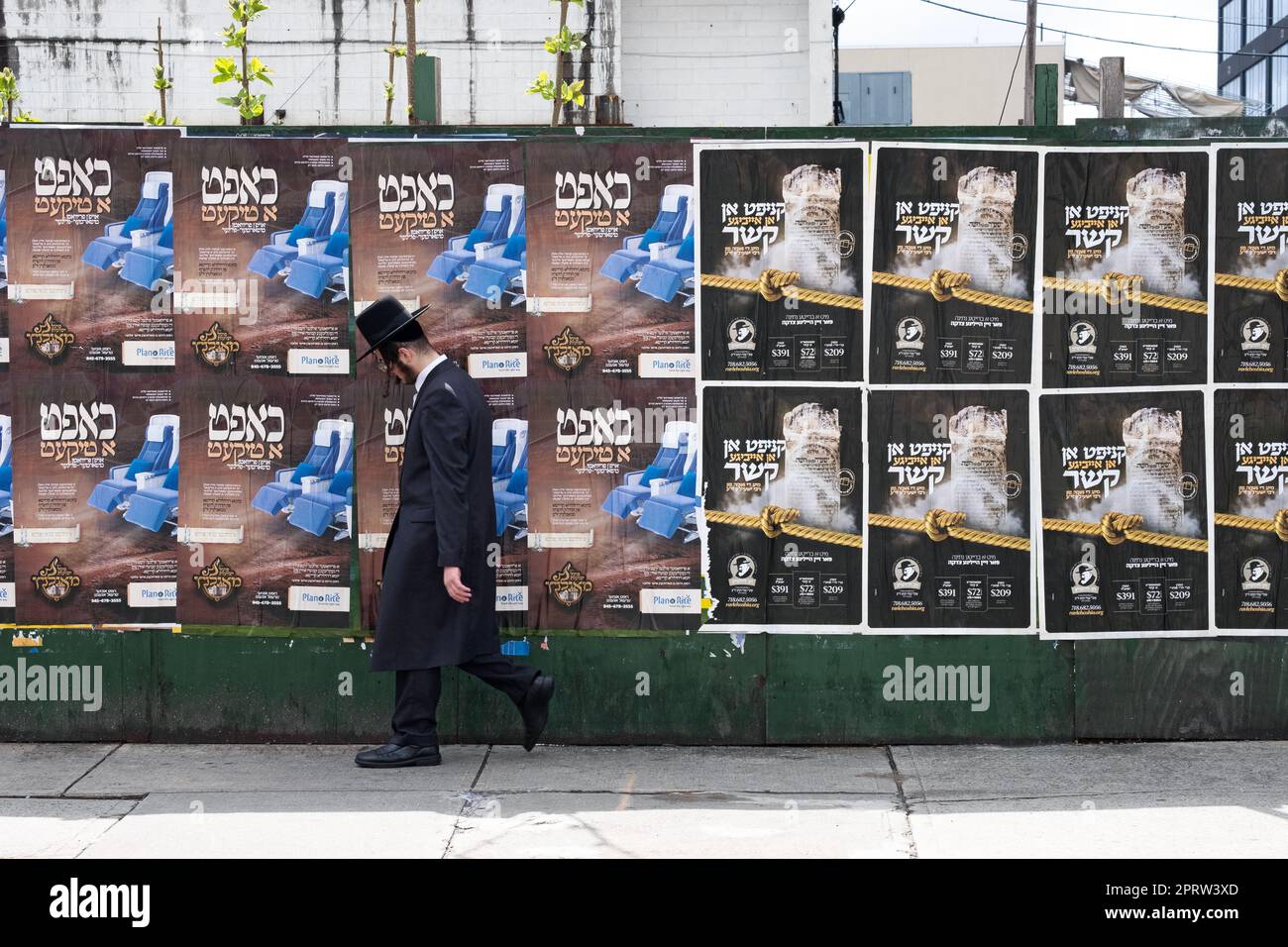 Ein orthodoxer Jude geht mit jiddischen Plakaten an einer Mauer vorbei, eines für ein 