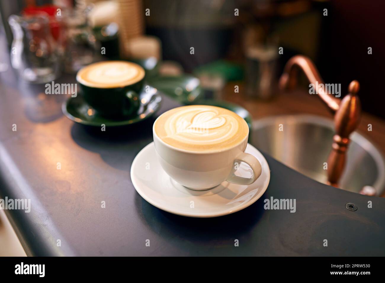 Café-Kultur. Hochgedrehte Aufnahme einer liebevoll zubereiteten Tasse Cappuccino, die auf einem Kaffeetisch sitzt. Stockfoto