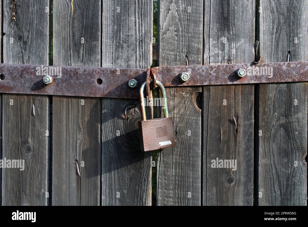 Vorhängeschloss braunes Metallschloss Nahaufnahme eines alten grauen Holztors. Stockfoto
