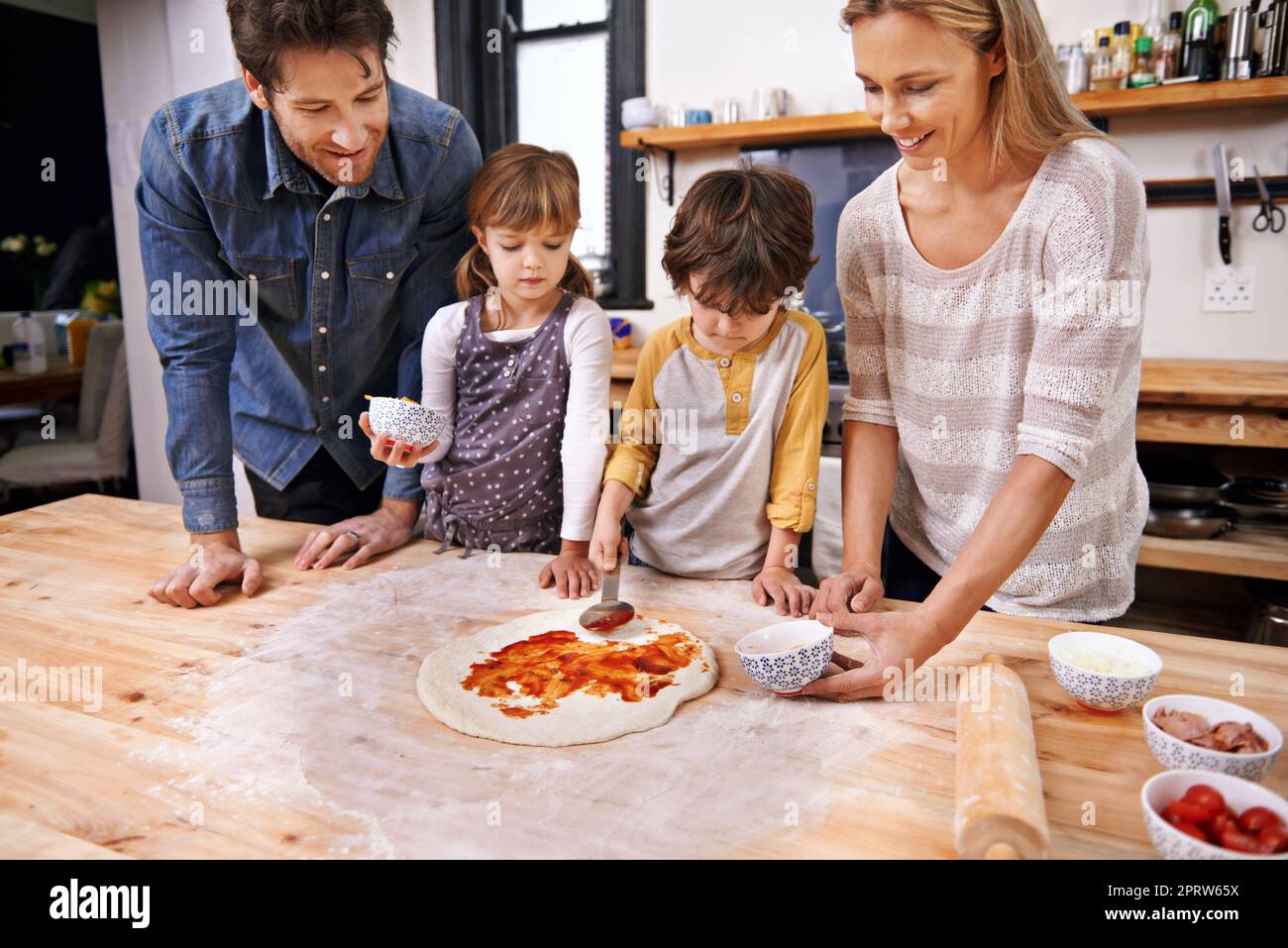 Die Tomatenbasis hinzufügen... Eine Familie, die zu Hause Pizza macht. Stockfoto