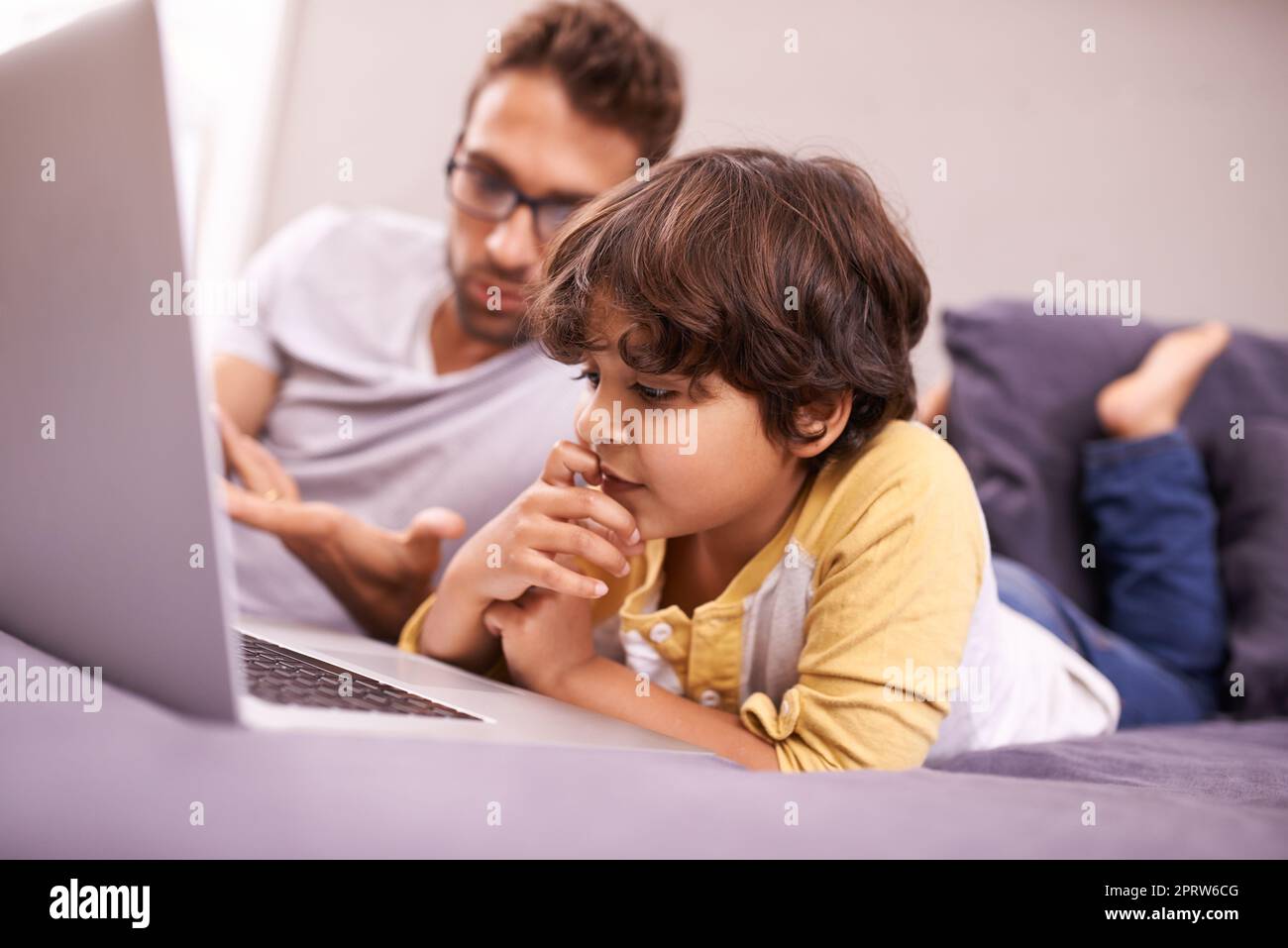 Wir spielen das Ratespiel. Ein Vater und Sohn mit einem Laptop, während sie auf dem Bett liegen. Stockfoto