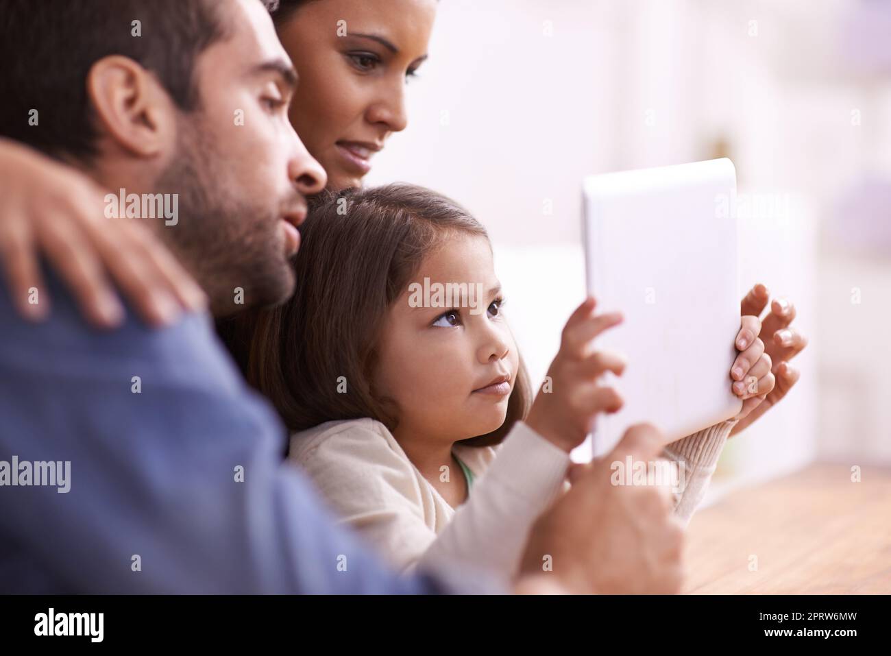 Zeit für Familienfilme. Ein kleines Mädchen, das mit ihren Eltern auf einem Tablet spielt. Stockfoto