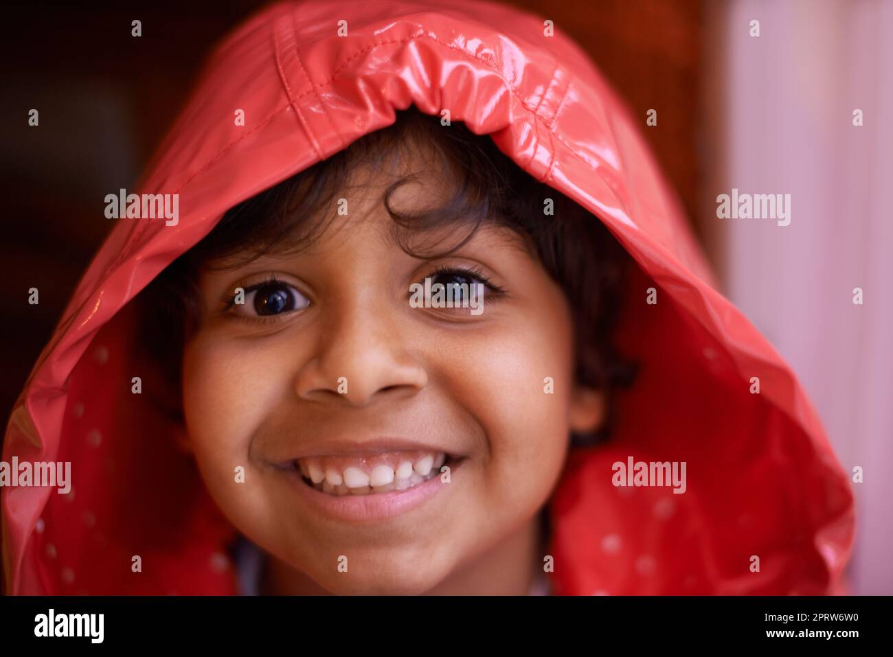 Immer spielen... auch im Regen. Ein begeisterter kleiner Junge trägt einen Regenmantel. Stockfoto