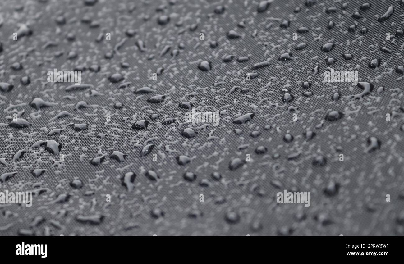 Regentropfen auf einer schwarzen metallischen Oberfläche in der Nahaufnahme. Stockfoto