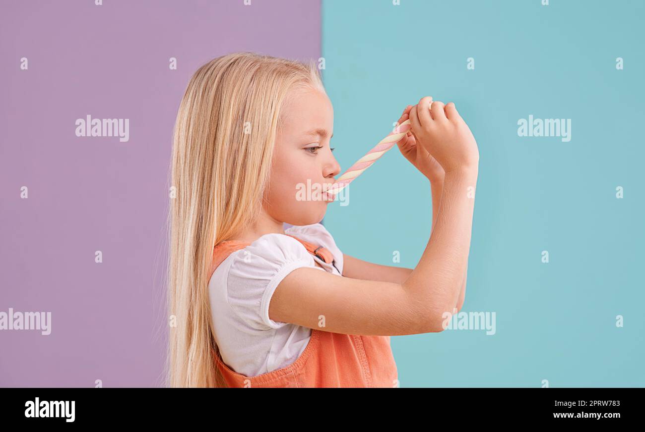 MMM, es ist so zäh. Ein nettes kleines Mädchen, das Süßigkeiten vor einem bunten Hintergrund isst. Stockfoto