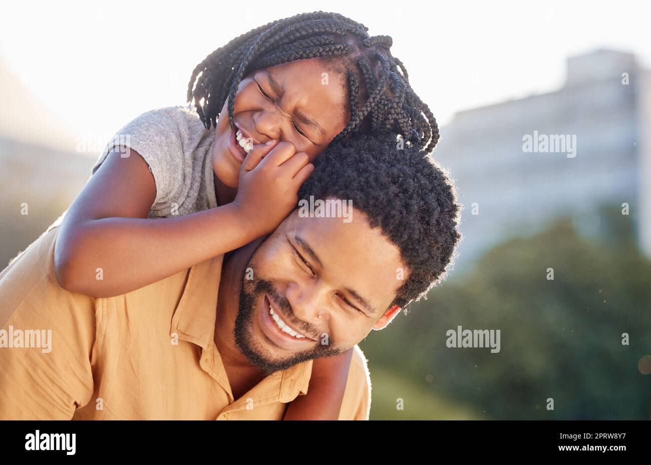 Glücklicher, schwarzer Vater und glückliche Tochter, die wieder fröhlich und freudig in die Natur hineinlächeln. Ein afrikanisches kleines Mädchen lächelt, lacht und genießt im Sommer draußen die Zeit mit dem fürsorglichen Vater Stockfoto