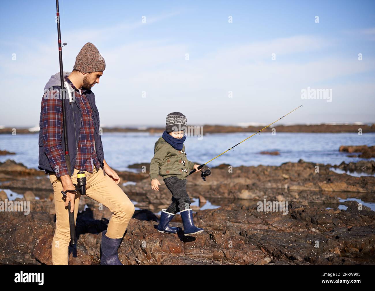 Ein Vater und ein Sohn gehen auf den Felsen, während sie zusammen am Meer fischen. Stockfoto