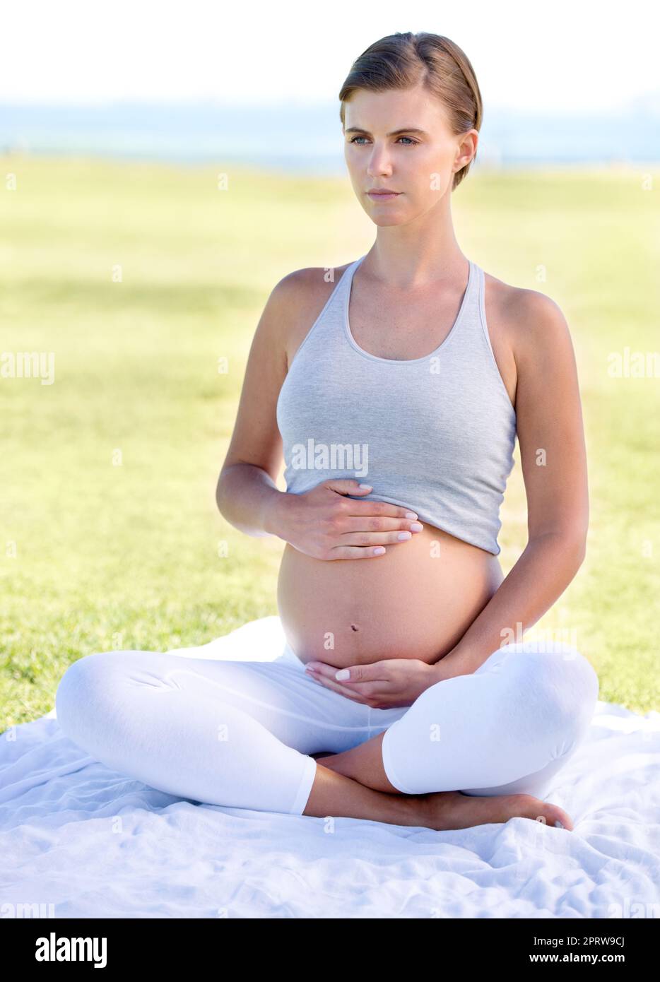 Bleiben in Spitzenform während ihrer Schwangerschaft. Eine schöne Schwangerin, die im Freien Yoga macht. Stockfoto