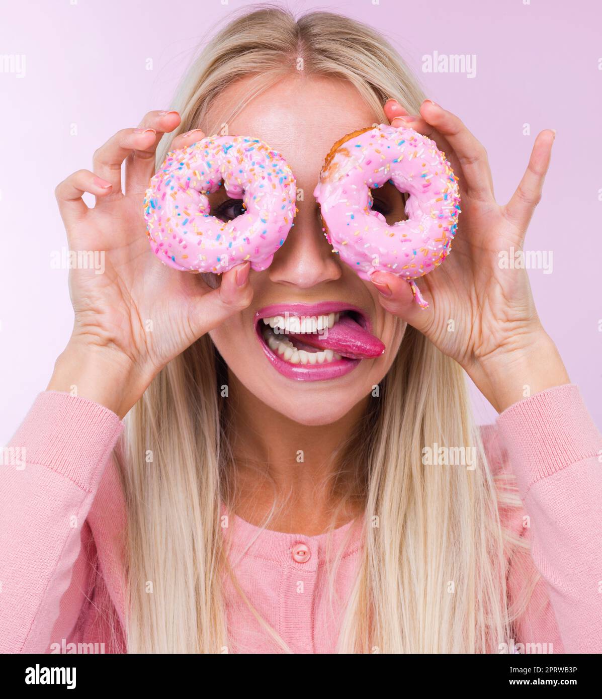 Eine Frau, die Donuts vor ihren Augen hält, während sie auf Rosa isoliert ist. Stockfoto
