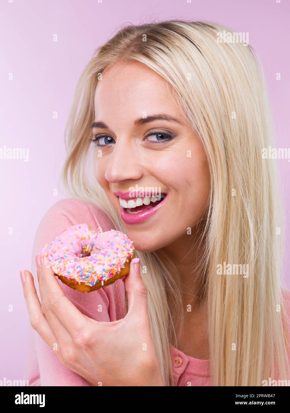 MMM.. Wer sagt, ich kann nicht frönen. Eine Frau, die einen Donut isst, während sie auf Rosa isoliert ist. Stockfoto