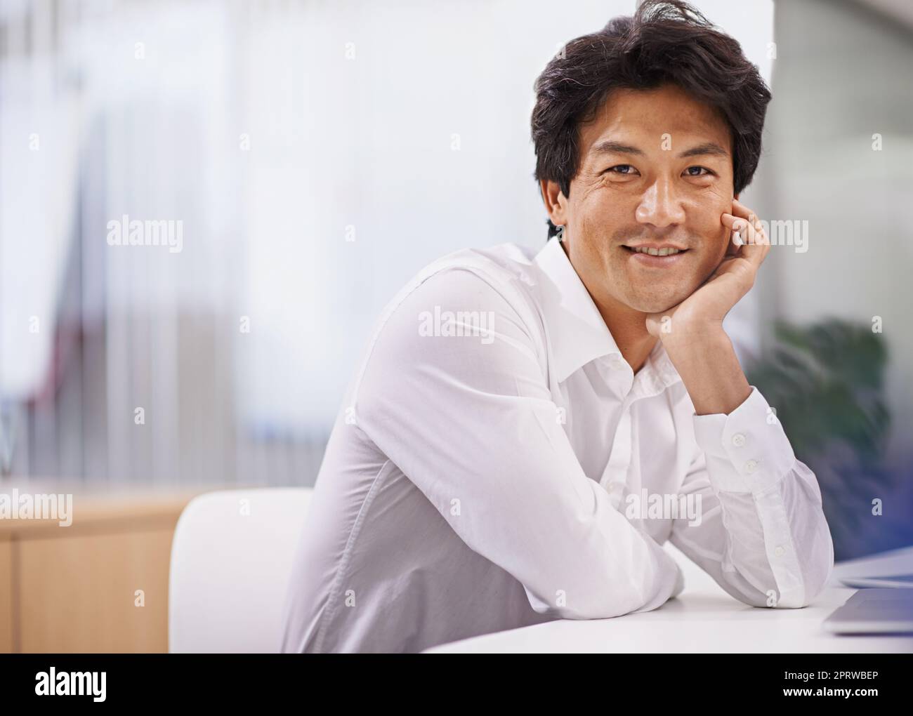 Das Unternehmen mit Geschick führen. Porträt eines hübschen asiatischen Geschäftsmannes, der an seinem Schreibtisch sitzt. Stockfoto