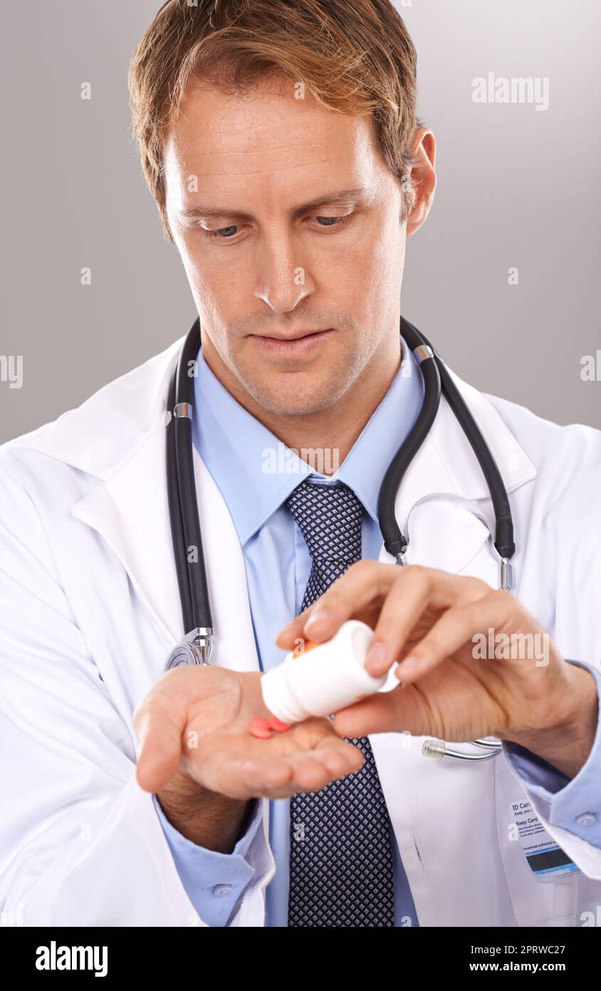 Ärzte bestellen für die empfohlene Dosis. Studioaufnahme eines hübschen Arztes, der Pillen aus einer Flasche auf seine Hand leerte. Stockfoto