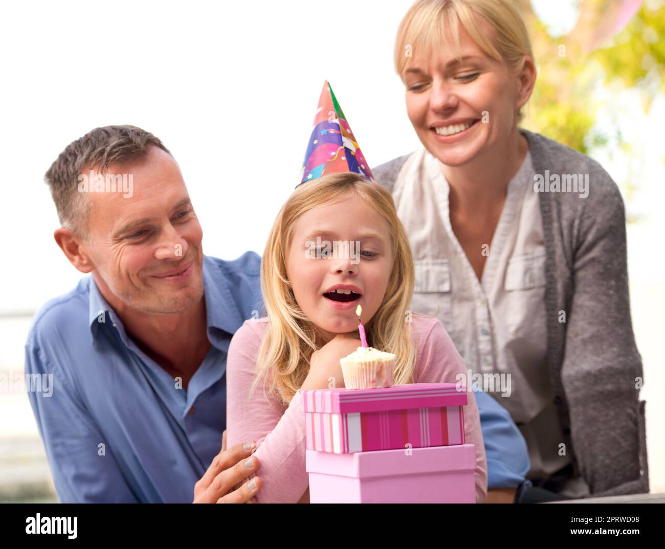 Machen Sie einen Wunsch. Eine kurze Aufnahme eines glücklichen Paares, das ihrem kleinen Mädchen zusieht, wie es an ihrem Geburtstag eine Kerze ausbläst. Stockfoto