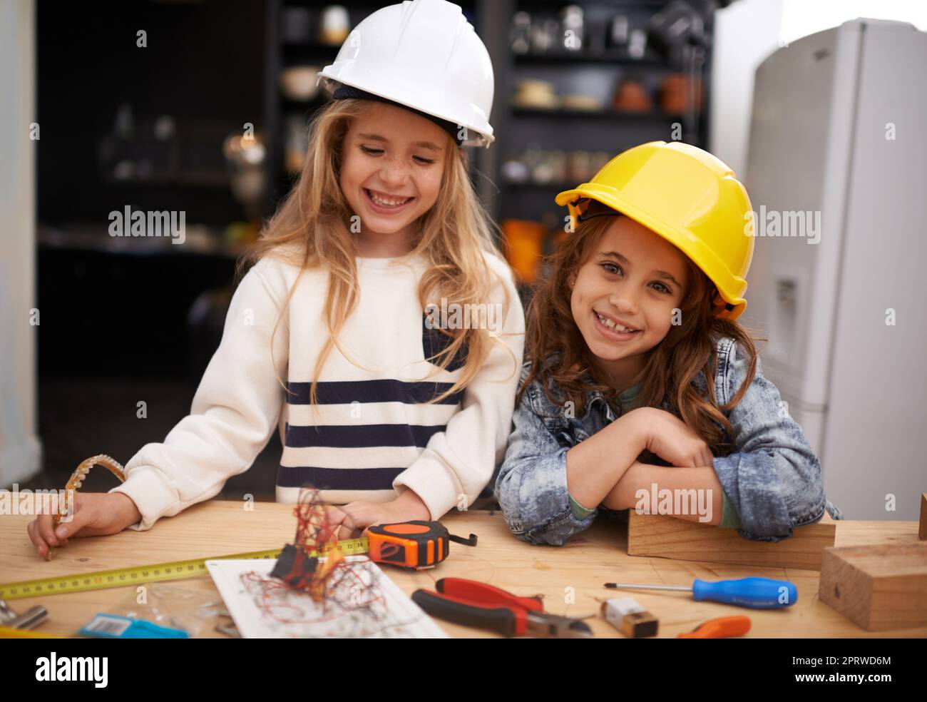Angehende kleine Erfinder. Zwei kleine Mädchen in Hüten, die zu Hause mit Werkzeugen spielen. Stockfoto