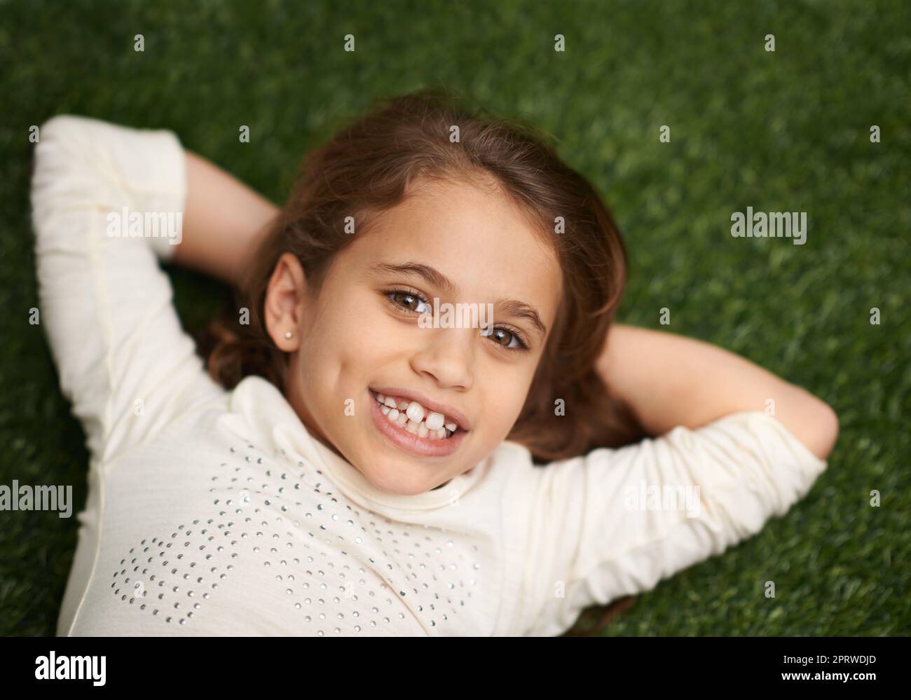 Unbeschwerte Kindheitstage. Hochwinkelporträt eines niedlichen kleinen Mädchens, das auf dem Rücken auf dem Gras liegt. Stockfoto
