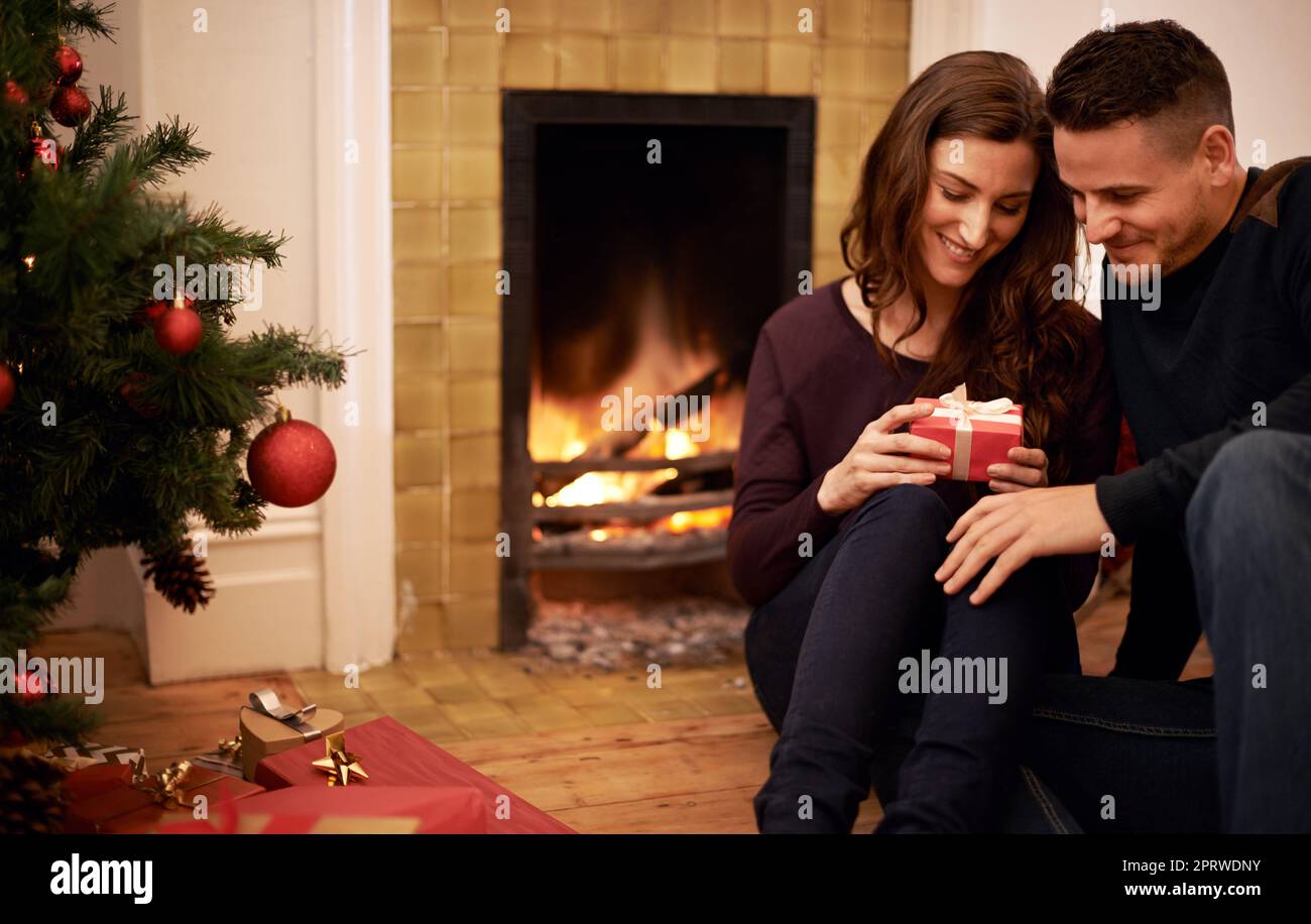 Wir feiern ein gemütliches Weihnachtsfest. Eine kurze Aufnahme eines jungen Paares, das Weihnachtsgeschenke austauscht. Stockfoto