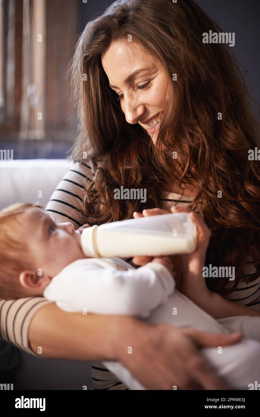Eine anbetende Mutter, die ihrem Baby eine Flasche schenkt. Stockfoto