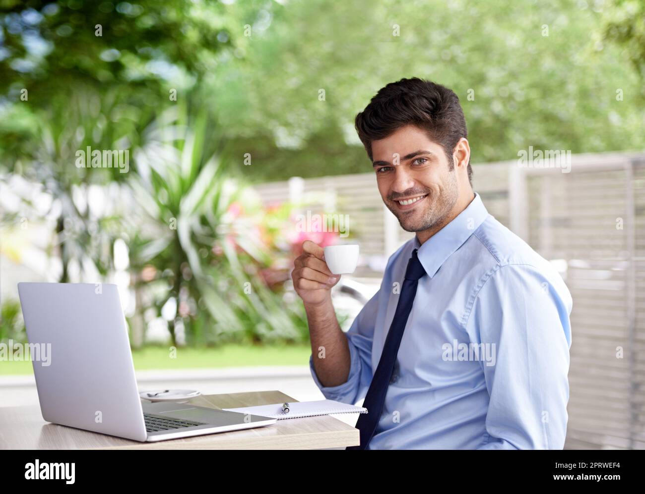 Espresso - meine Geheimwaffe. Ein hübscher junger Geschäftsmann, der im Freien an seinem Laptop arbeitet. Stockfoto