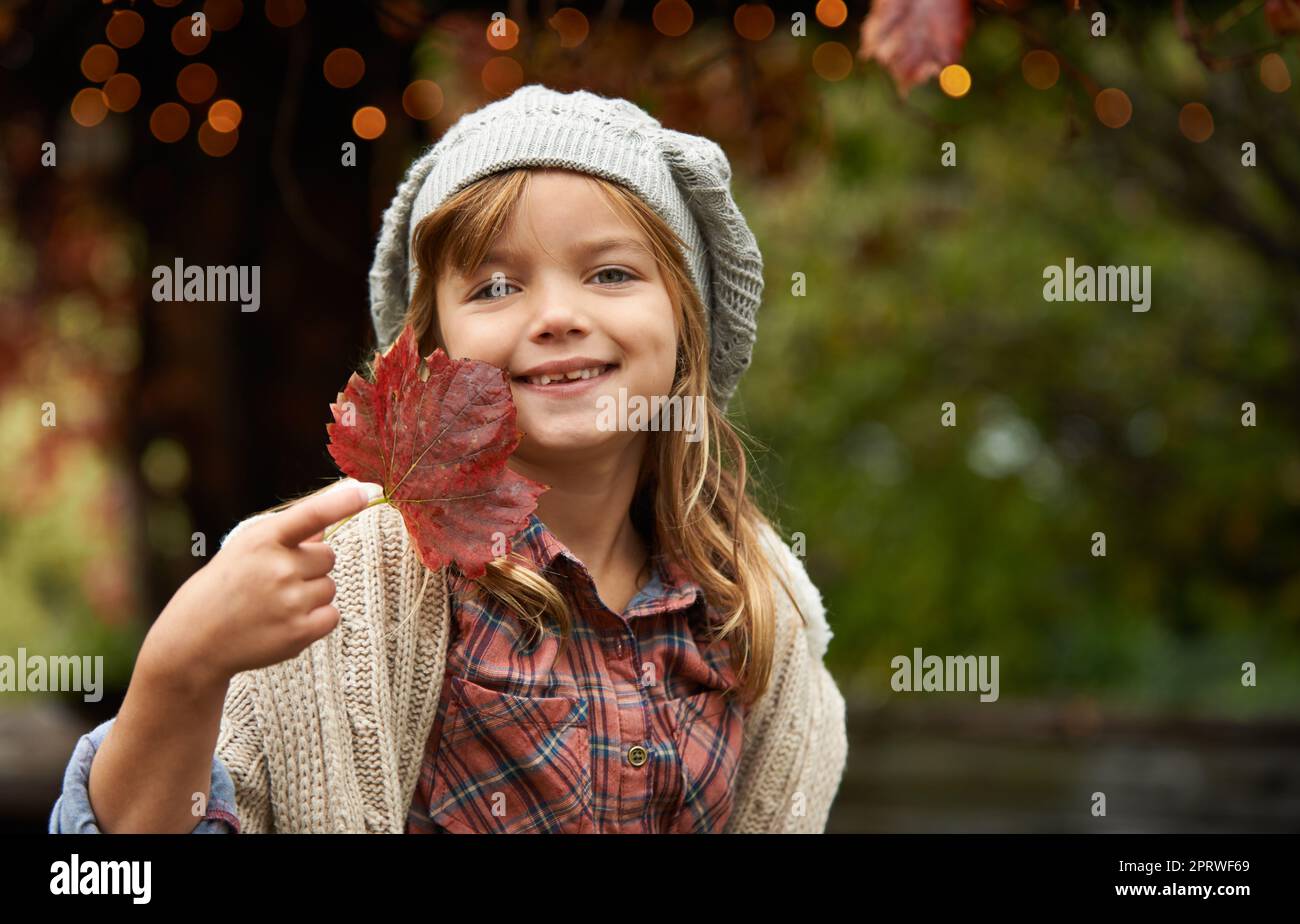 Seht, wie schön es ist. Porträt eines niedlichen kleinen Mädchens mit einem Herbstblatt shes im Garten gefunden. Stockfoto