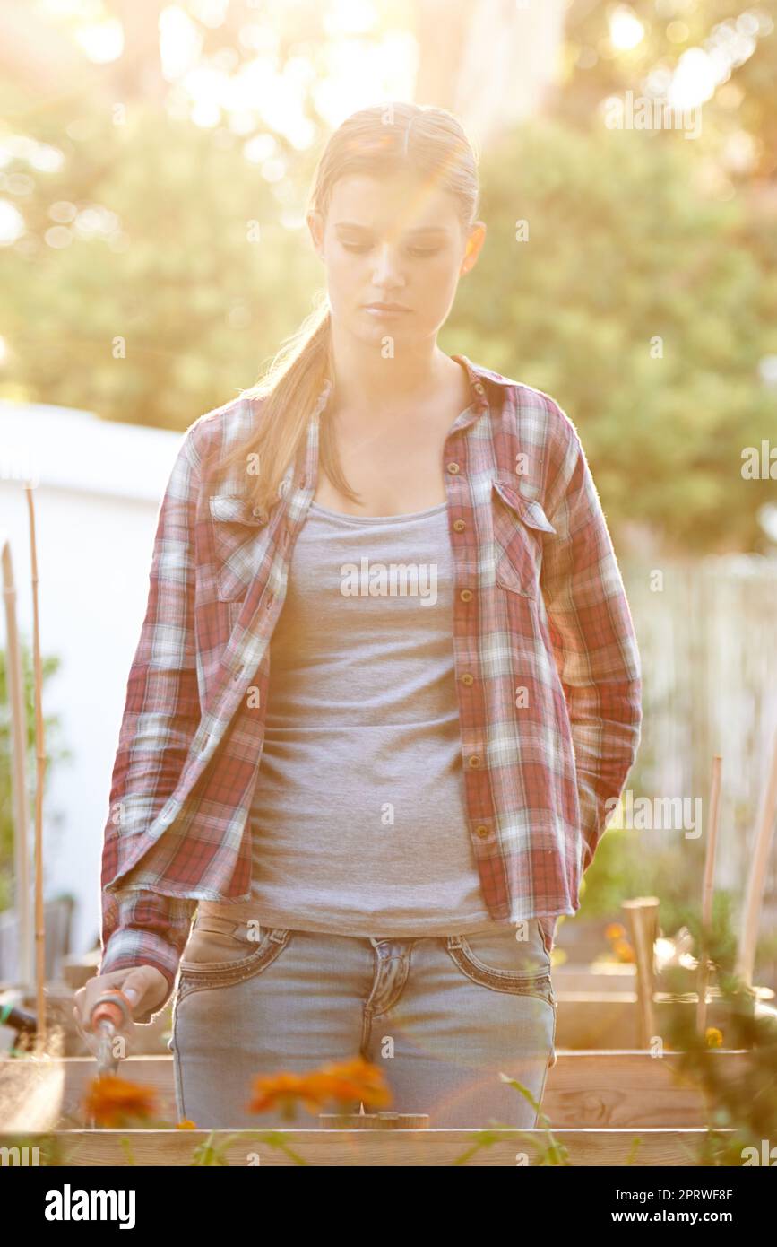 Wenn das Leben gibt Ihnen Schmutz wachsen einen Garten. Eine schöne junge Frau Gießen ihre Pflanzen draußen. Stockfoto