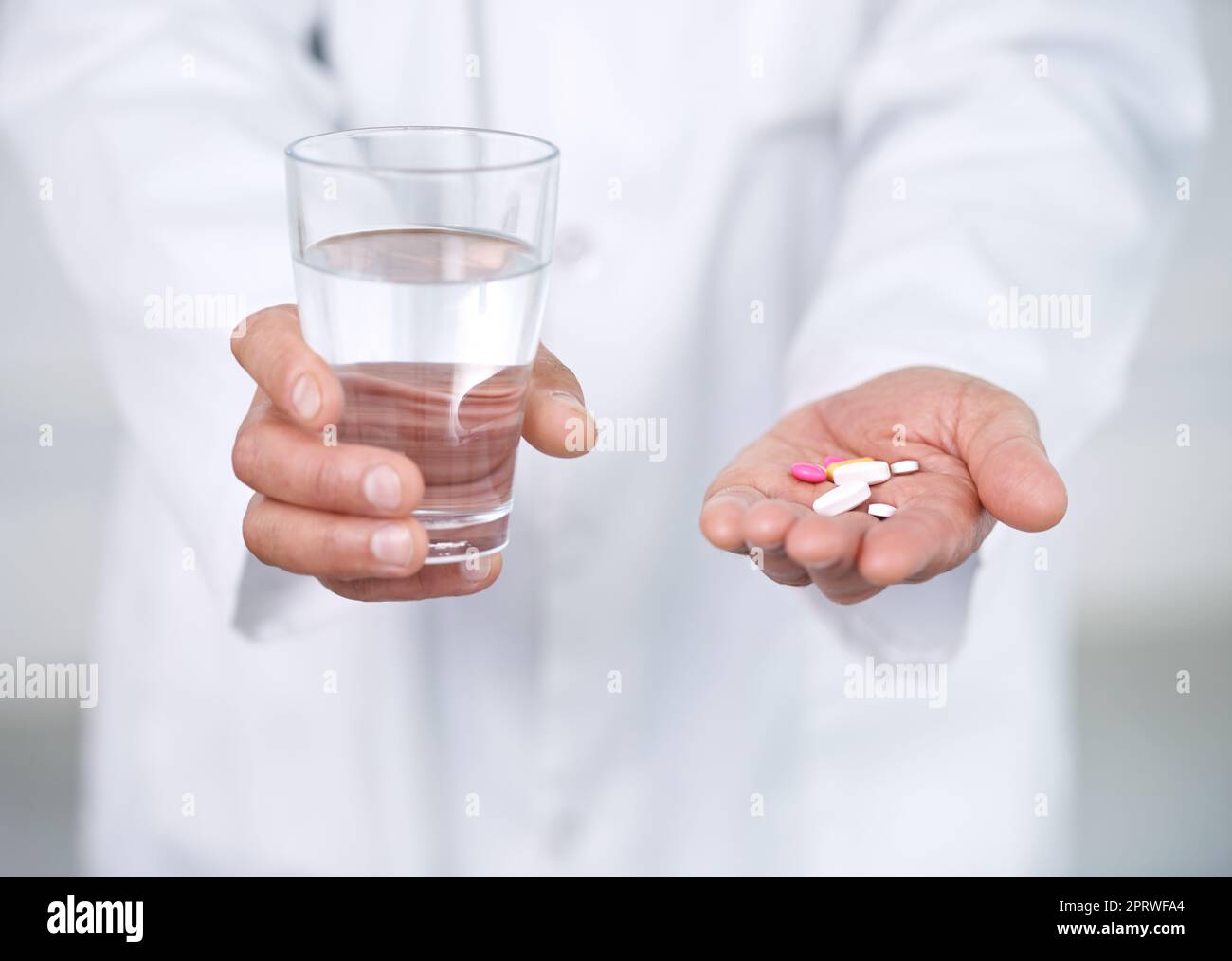 Nehmen Sie zwei davon und rufen Sie mich am Morgen. Ein Arzt hält ein Glas Wasser in der einen Hand und Medikamente in der anderen. Stockfoto