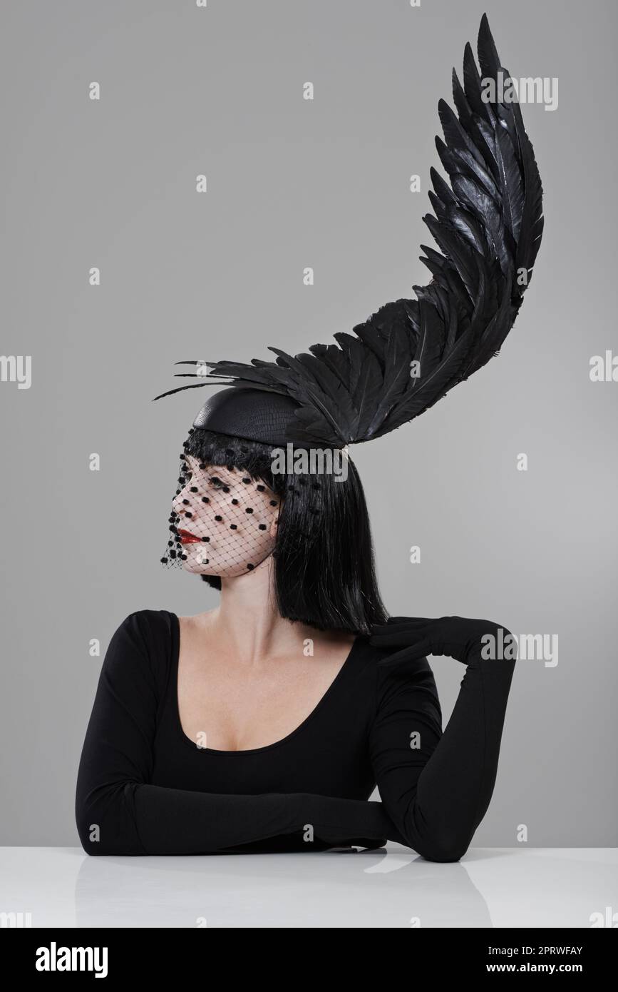 Gefiederte Mode. Eine junge Frau in einem flügelförmigen Kopfteil, die in einem Studio sitzt. Stockfoto