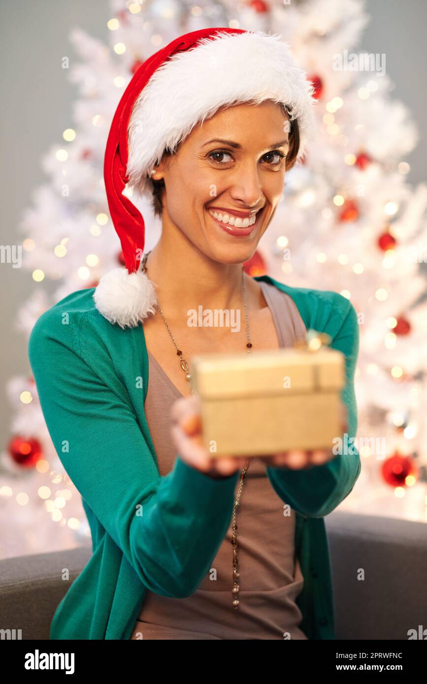 Für Sie. Eine schöne junge Frau, die eines ihrer Weihnachtsgeschenke der Kamera zeigt. Stockfoto