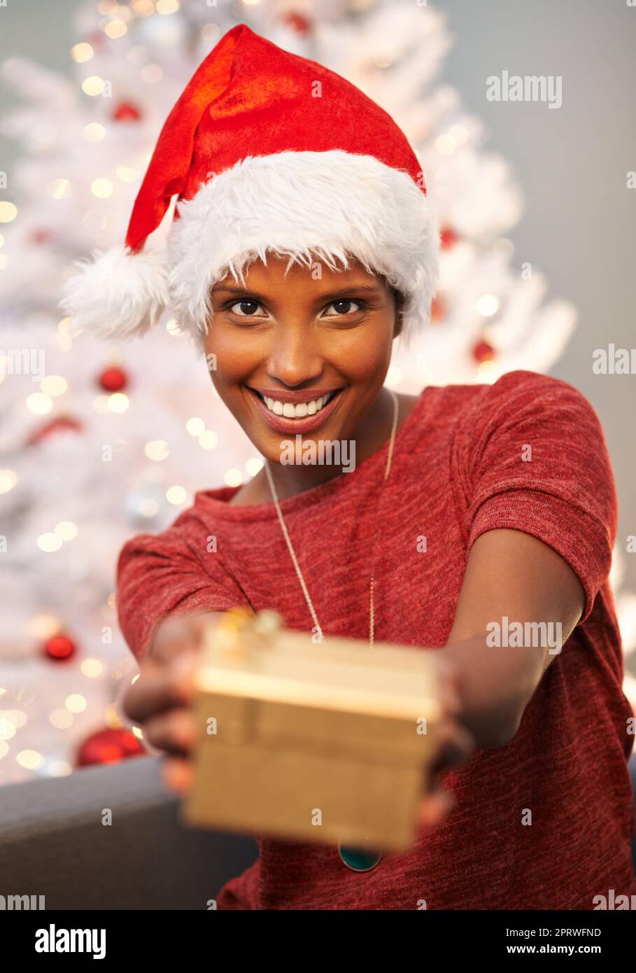 Das ist für Sie. Eine schöne junge Frau, die eines ihrer Weihnachtsgeschenke der Kamera zeigt. Stockfoto