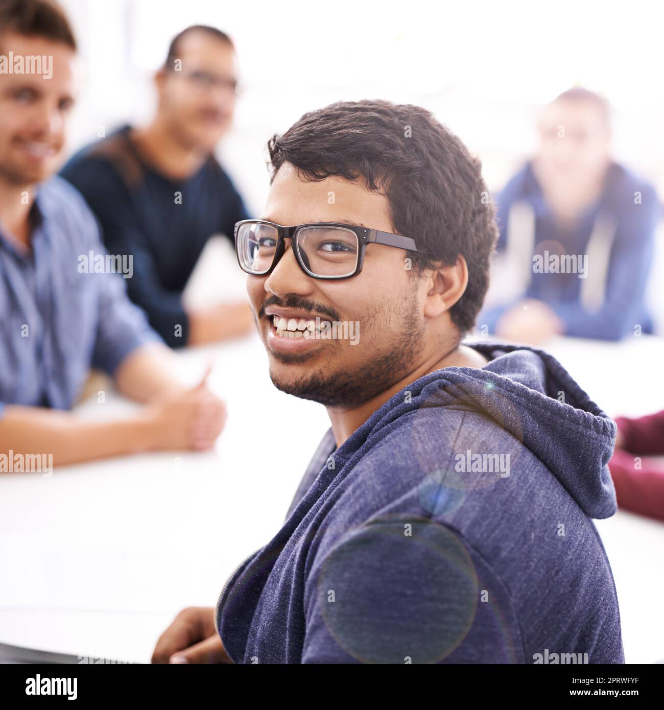 Ihr Traum-Technikteam. Porträt eines glücklichen jungen Mannes, der bei einem Treffen mit seinen Kollegen sitzt. Stockfoto